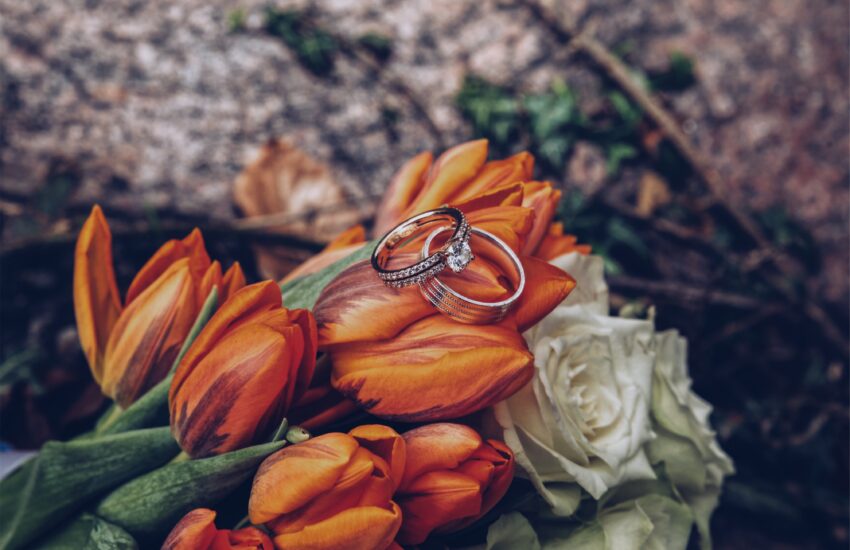 A selective closeup shot of silver diamond engagement rings on orange tulips and white roses